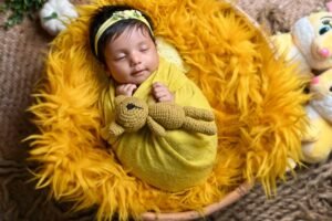 Sleeping newborn baby wrapped in a yellow blanket on a golden furry backdrop during a professional newborn photoshoot.