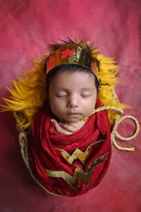 Sleeping newborn baby in a red and gold superhero costume during a creative newborn photoshoot at Mamma's Tiny Cubberry.